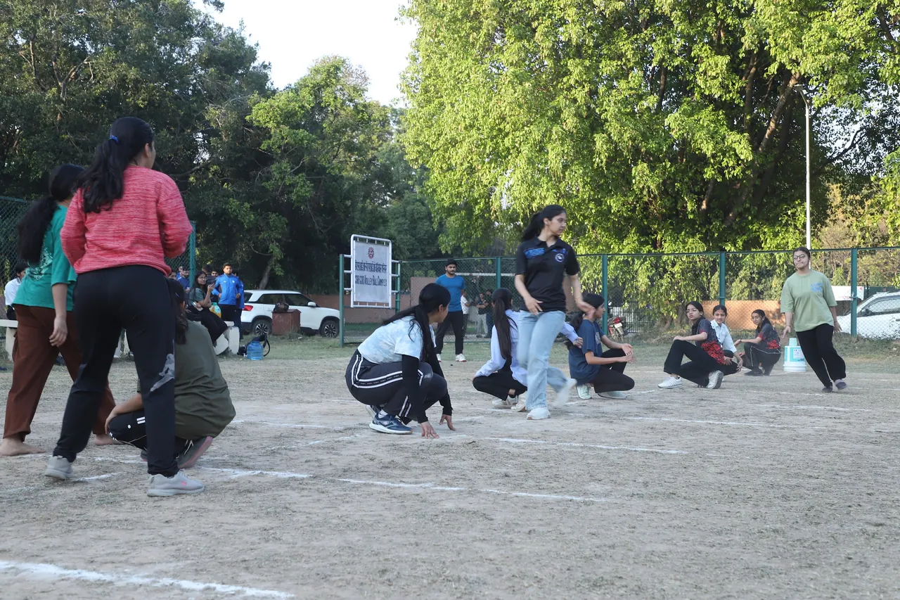 Kho kho players crouched in a line as the chaser runs