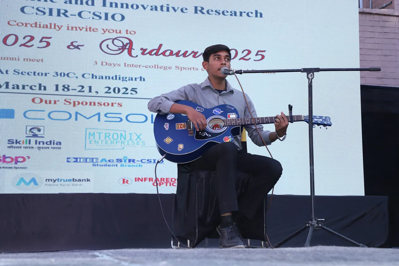 A guitarist plays seated on the outdoor stage