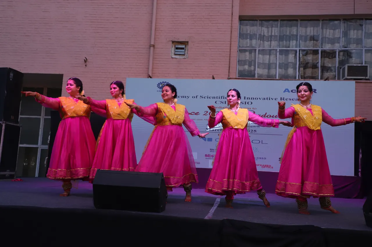 A group of dancers in pink and yellow perform in formation