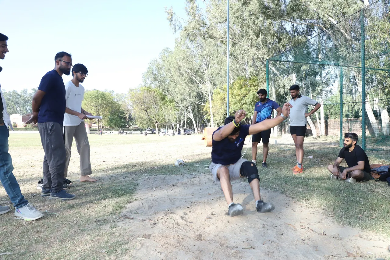 An athlete lands in the long jump pit as officials watch