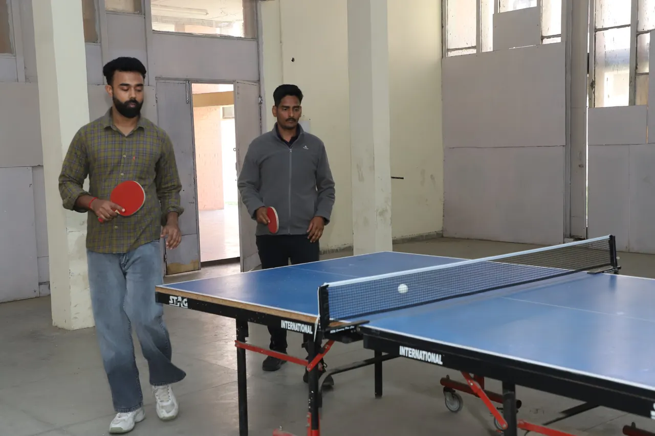 Two table tennis players in a rally at the indoor tables