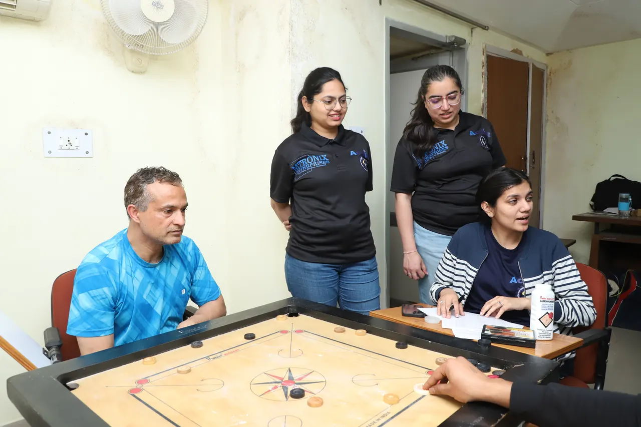 Players and onlookers gather around a carrom board