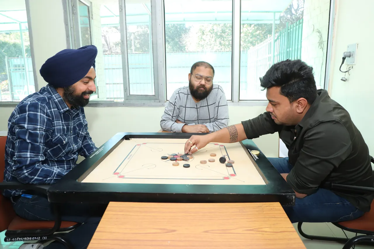 Three players concentrate around a carrom board