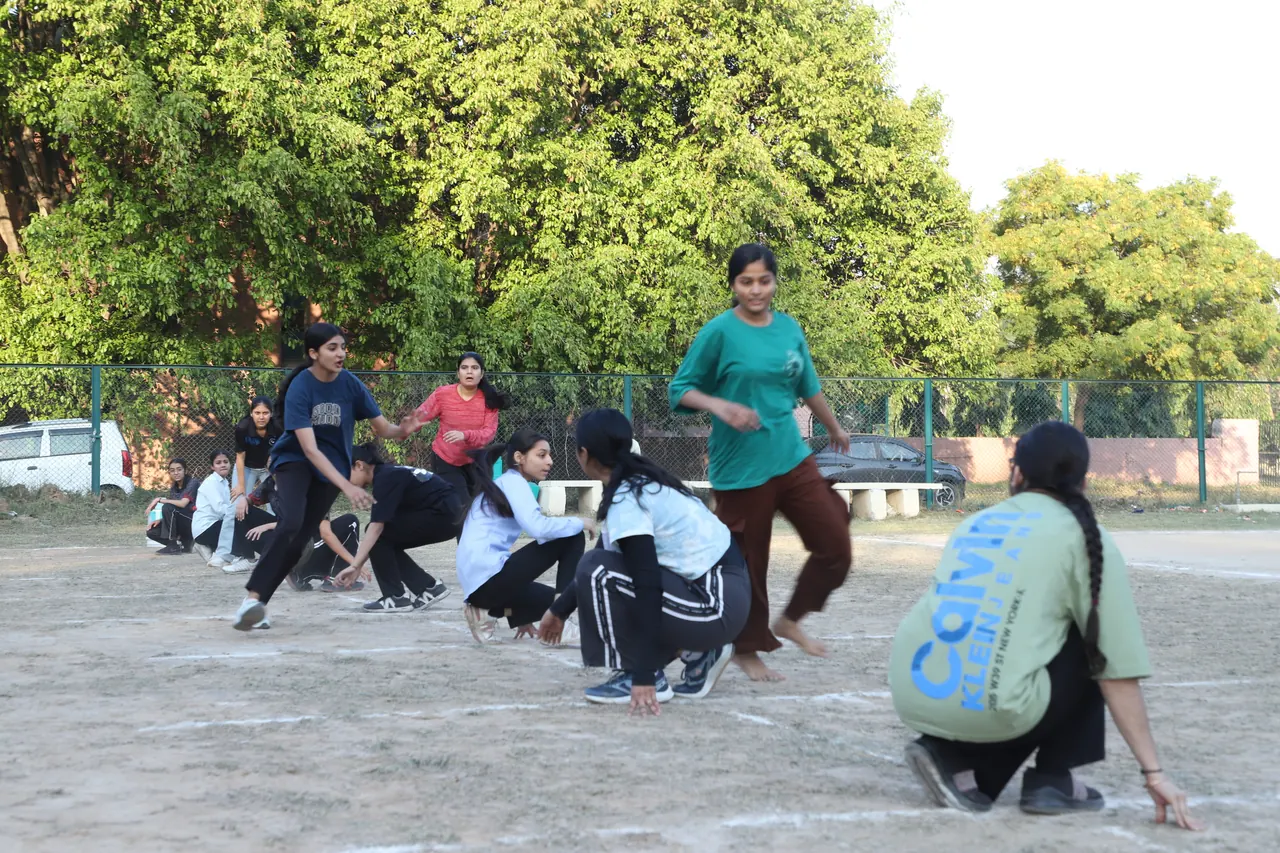 Kho kho players crouch in a line while a chaser runs past