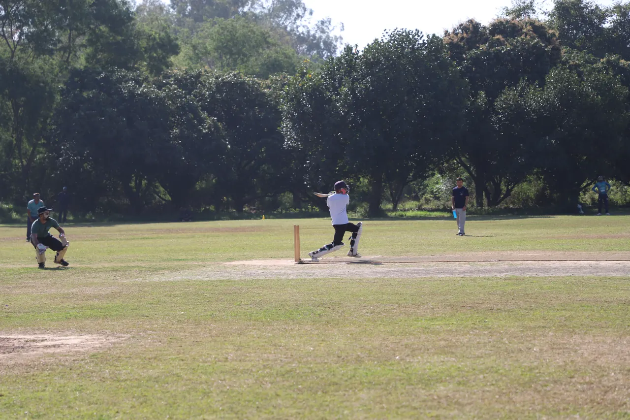 A batter plays a shot as fielders watch on the cricket ground