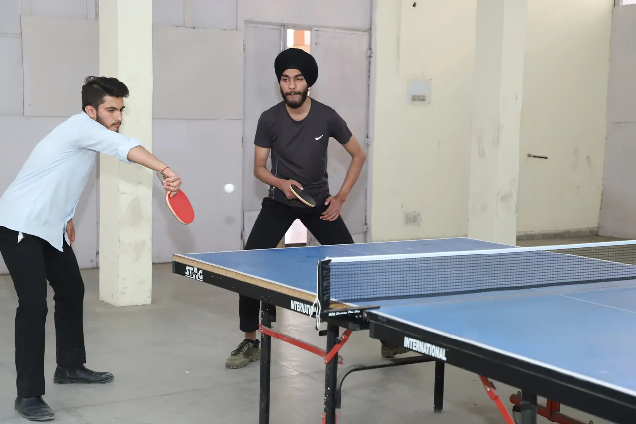Two table tennis players reach for the ball across the net