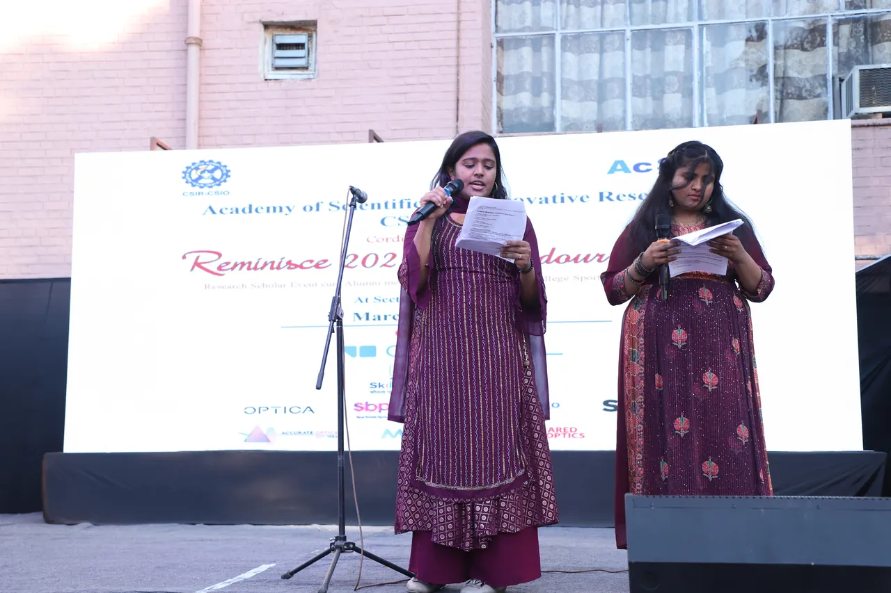 Two hosts read from their scripts on stage