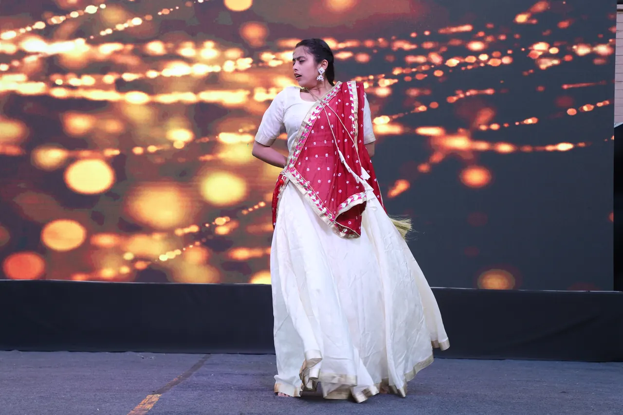 A dancer in a white and red outfit performs on stage in front of a glowing backdrop
