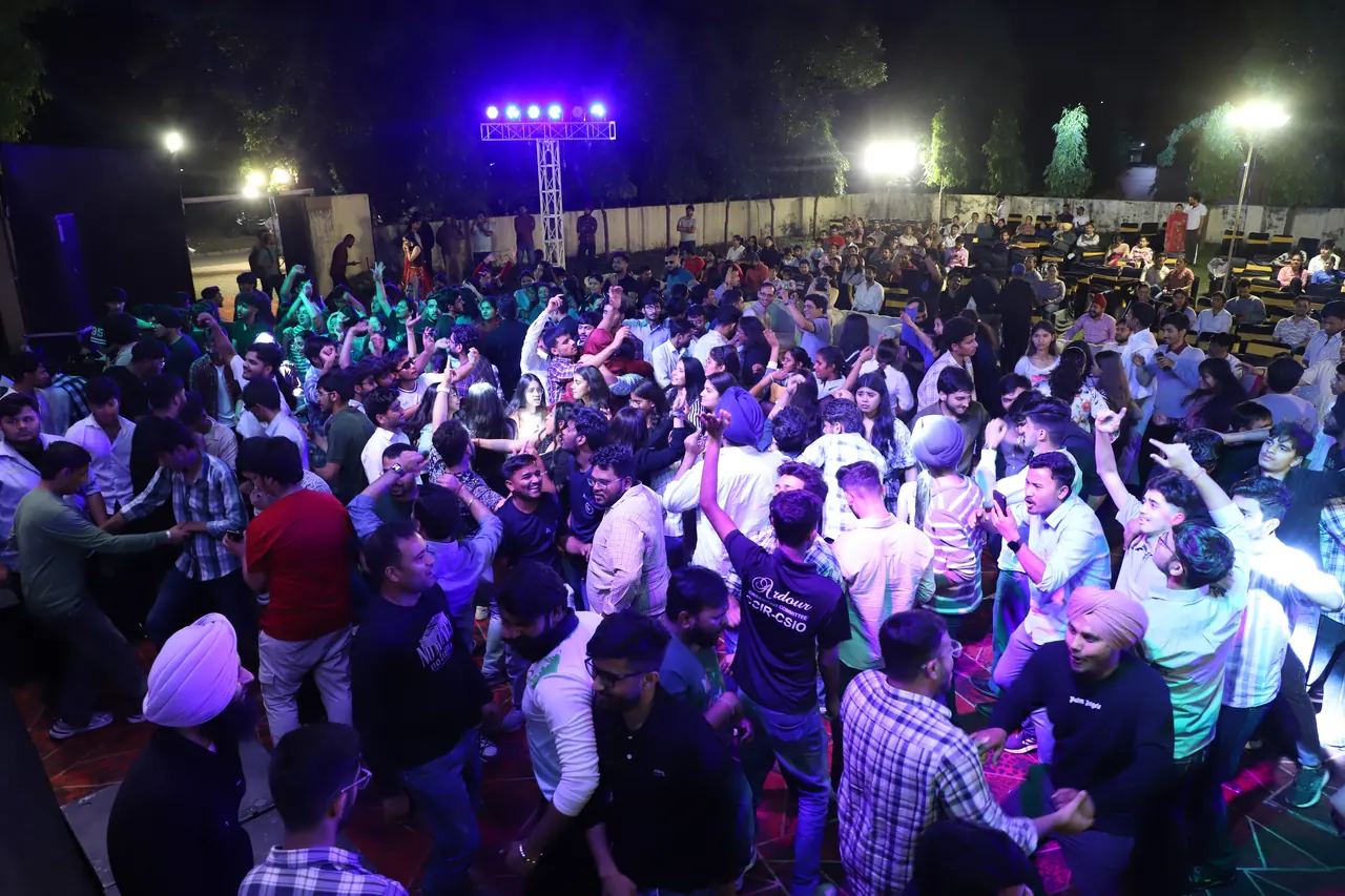 A large crowd dances under coloured stage lights at the evening programme