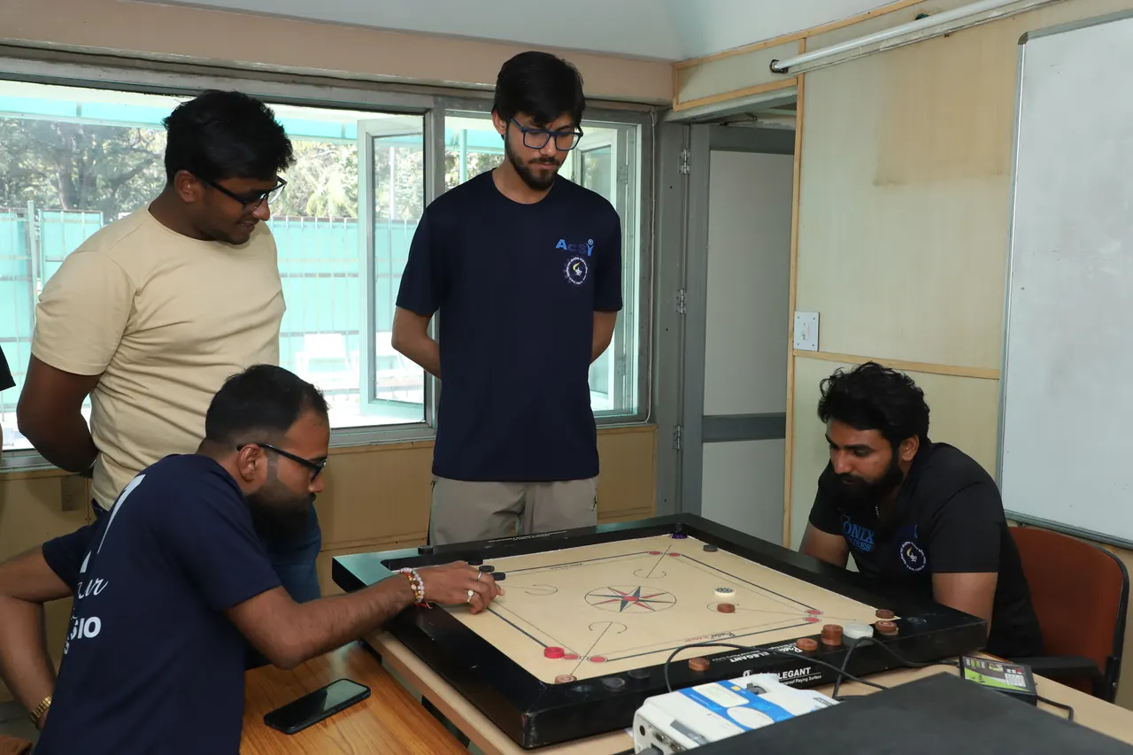 A player takes a shot while others watch the carrom board