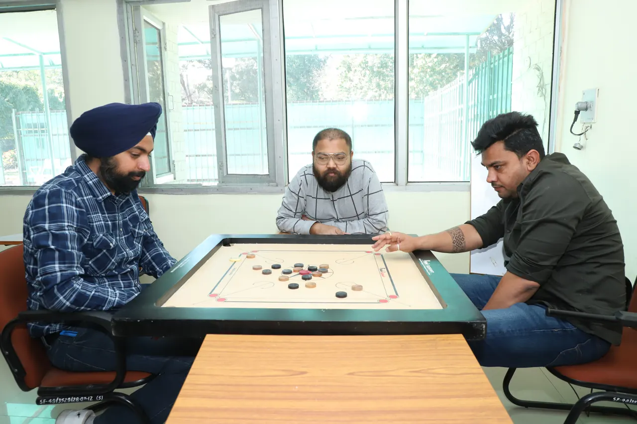 Three players around a carrom board