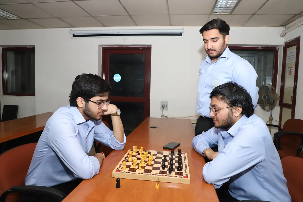 Two players at a chessboard as a third watches