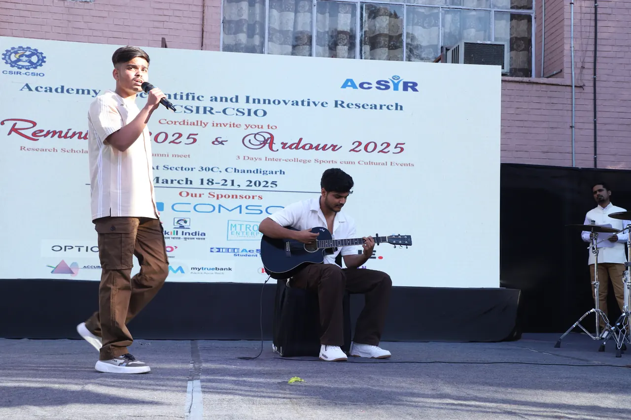 A performer with a microphone and a guitarist on the outdoor stage