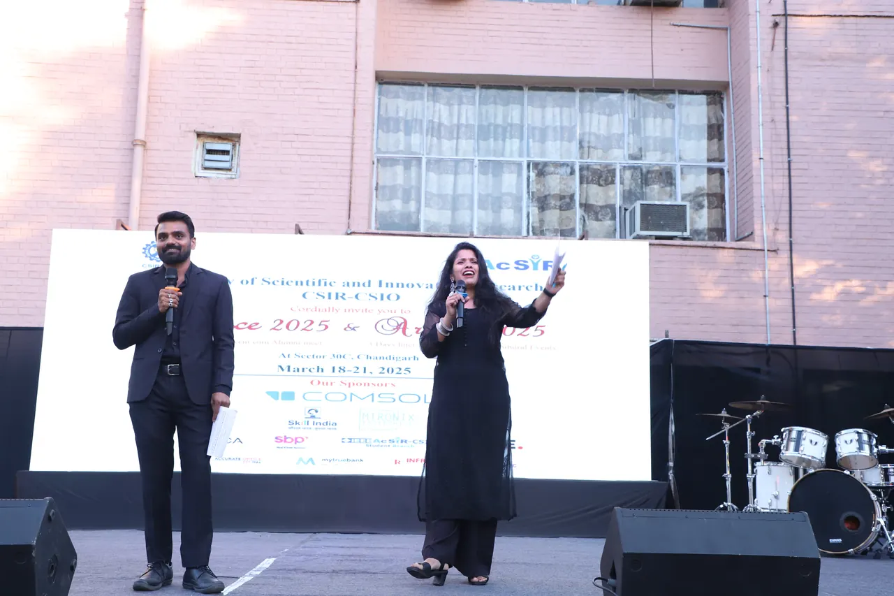 Two hosts on stage in front of the event backdrop