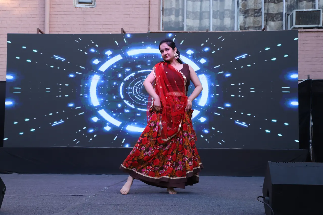 A dancer in red performs in front of a glowing ring backdrop
