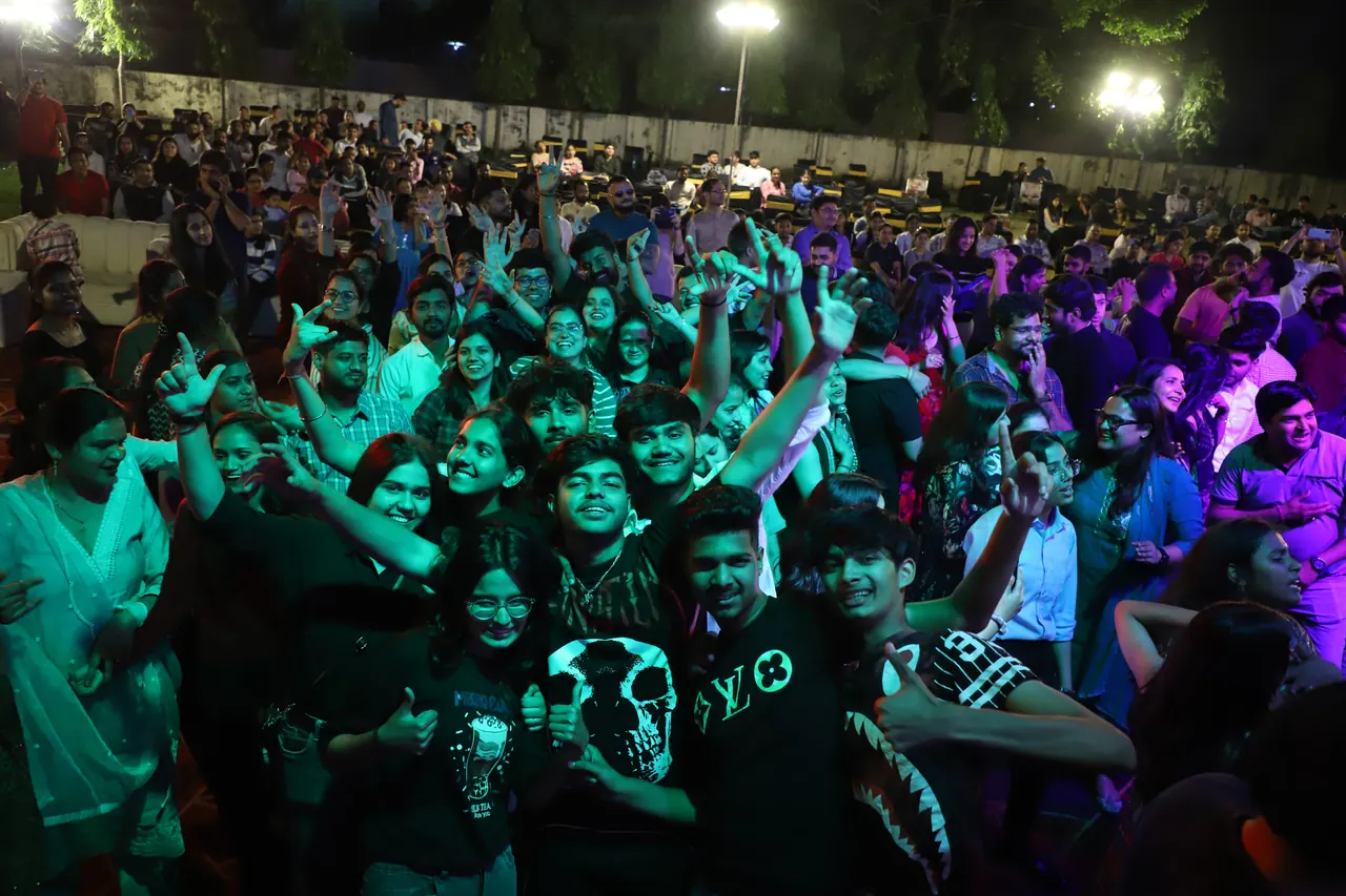 A large crowd dances under green and purple lights