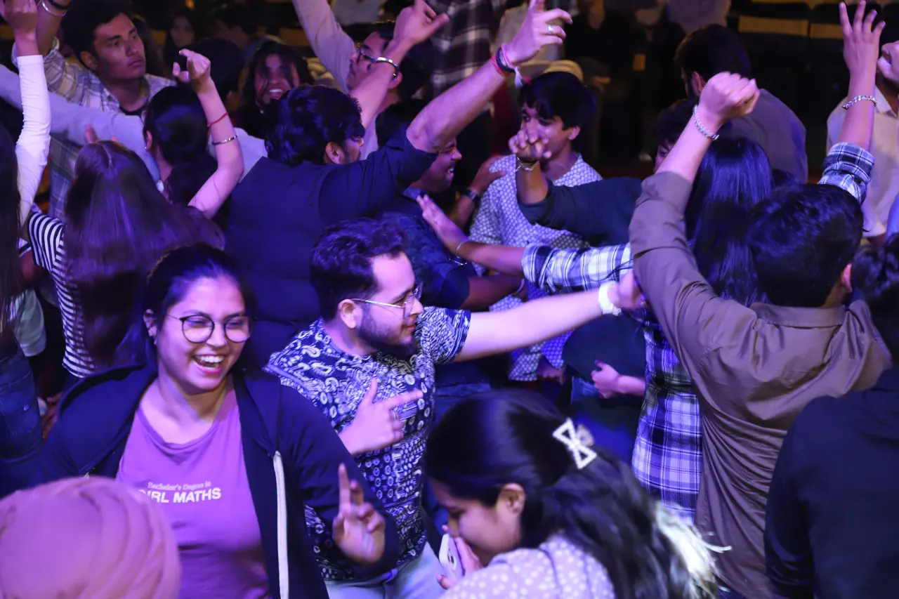 Participants dance with raised arms under purple light