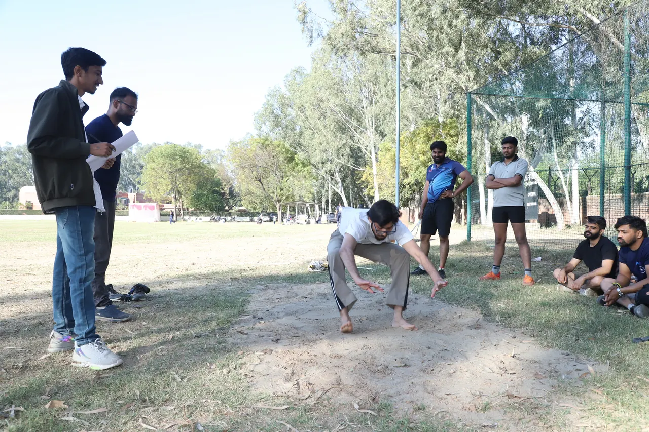 An athlete lands in the sand pit as others watch