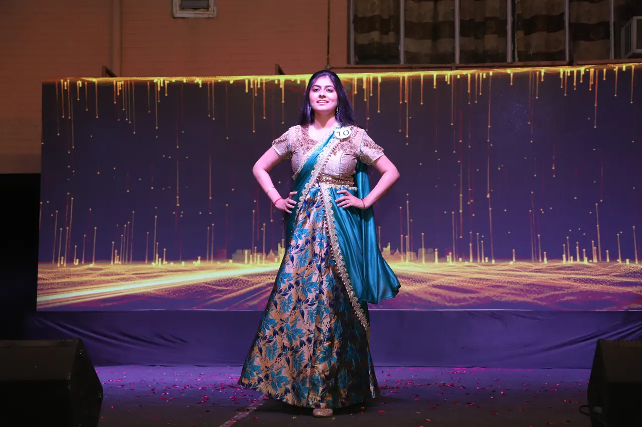 A participant in a teal and gold lehenga poses on the ramp