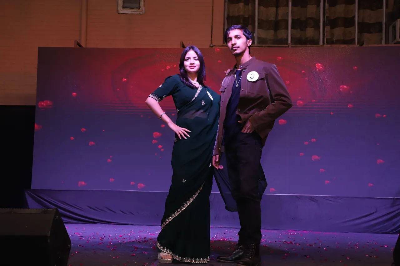 Two participants pose together on stage against a red backdrop